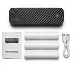 Vue d'ensemble d'une imprimante thermique portable A4 noire sur fond blanc, disposée au-dessus de ses accessoires : un manuel d'utilisation en français, trois rouleaux de papier thermique et un câble USB blanc.